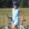 photo of woman standing with her bicycle in front of a grassy meadow backed with trees